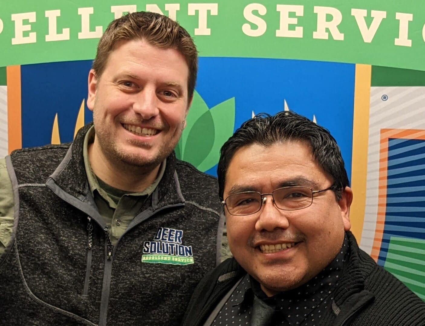 Kris Goodrich, Co-Founder of Deer Solution, standing next to new franchisee Victor Pariona, both smiling in front of a Deer Solution logo backdrop.